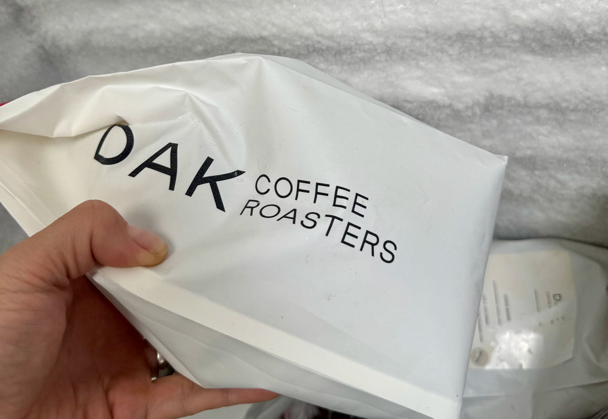 A hand holding a white DAK Coffee Roasters bag.